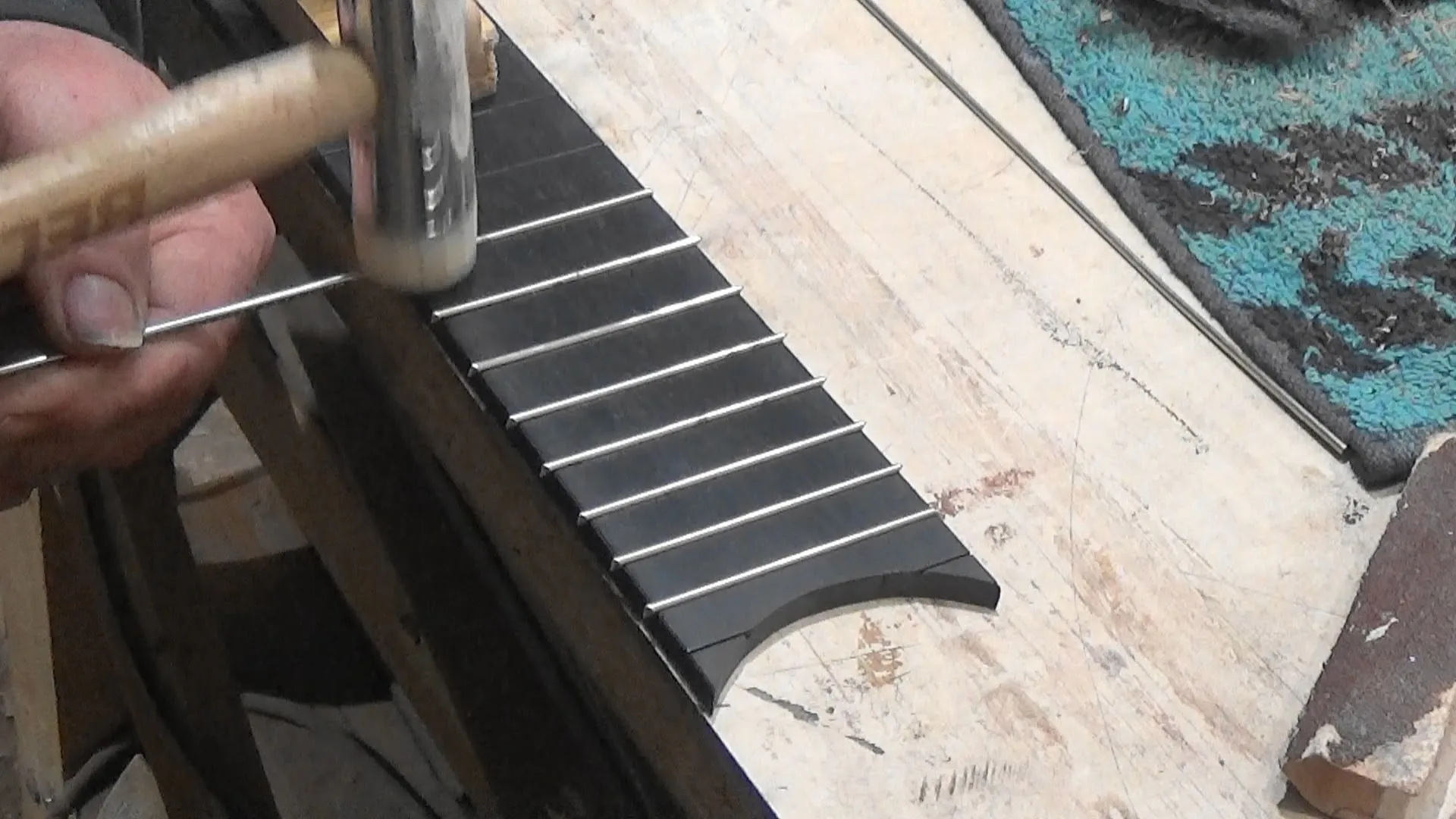 Mãos de luthier assentando traste em escala de ébano com martelo específico de luthieria, mostrando traste encaixado a partir do centro