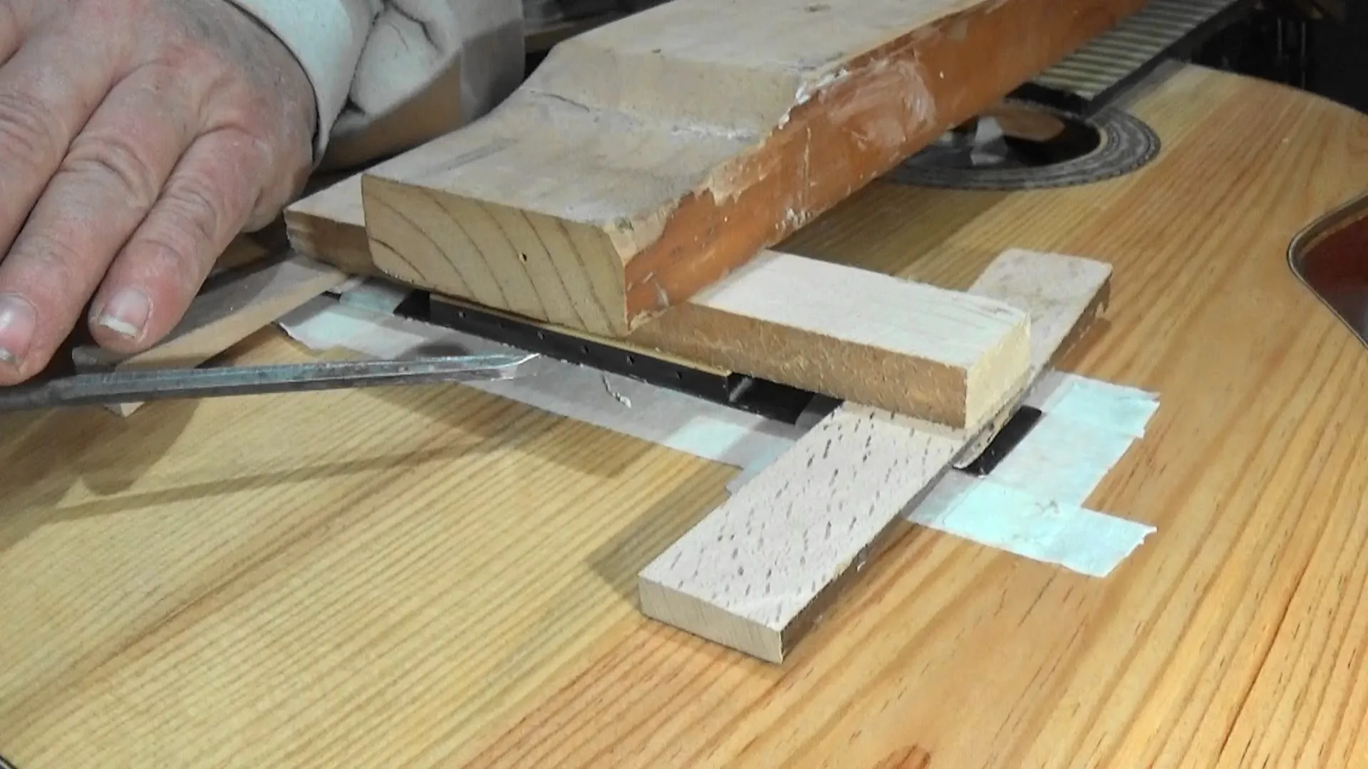Cavalete de violão sendo colado com grampos específicos de luthieria, com proteções de madeira no tampo para distribuir pressão