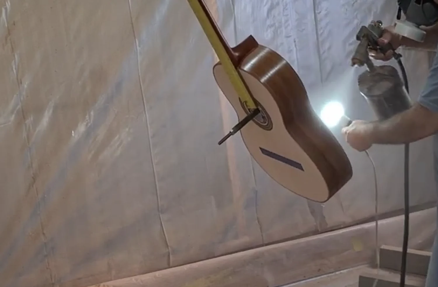 Aplicação de verniz nitrocelulose com pistola HVLP em cabine de pintura sobre lateral de violão
